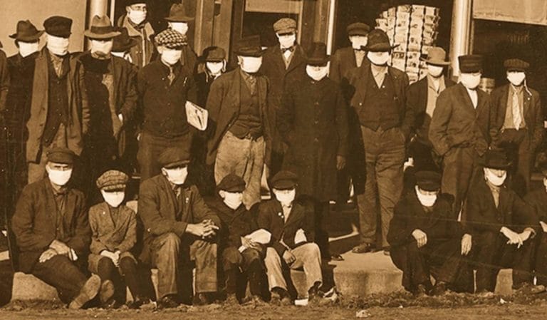 Men and boys posing for a photo outside, all wearing surgical masks.