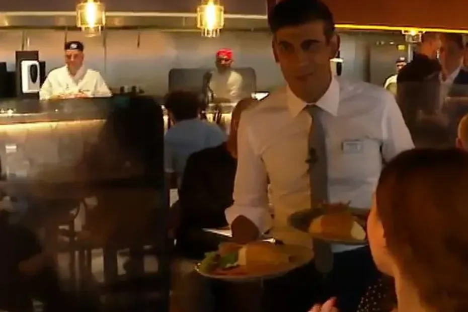 A grinning Rishi Sunak offering plates of food to people in restaurants as a virus rages.