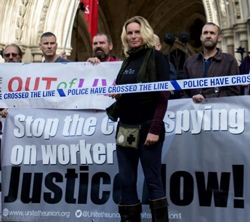 A woman with fair hair outside a courthouse flanked by activists holding banners.