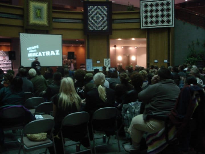 A hall with a seated audience before a screen that says "Escape from Doncatraz."