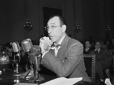 Herbert Biberman sat with hands clenched together, before a microphone, under questioning by HUAC.
