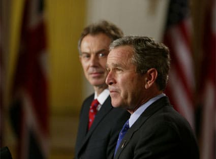 George W. Bush Jr speaking beside Tony Blair, who is gazing at him.