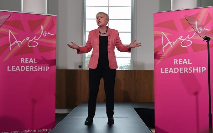 Angela Eagle gesticulates between two "Angela" banners said by many to resemble perfume branding.